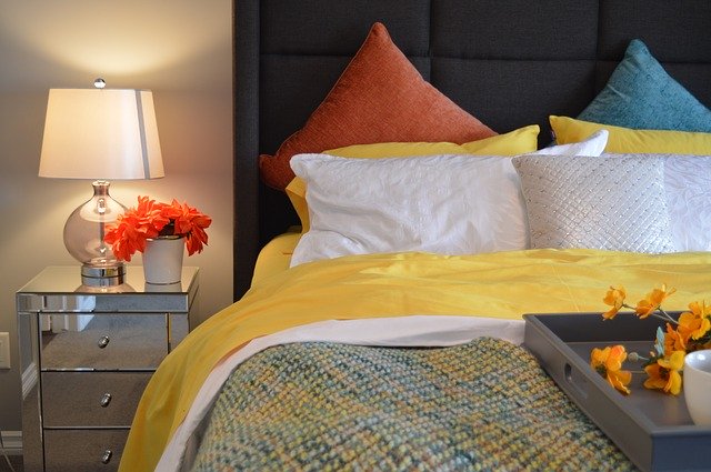 postel, bílé, žluté polštáře v pozadí ještě modrý a oranžový